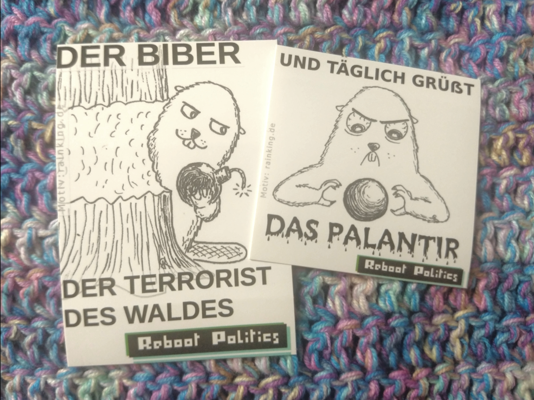 Zwei Sticker auf einer bunten Häkeldecke. auf dem Linken ist ein Biber mit einer Bombe in der Hand und schelmischen Blick abgebildet, der hinter einem angeknabberten Baum hervor schaut. Zu Lesen ist auf dem Sticker: Der Biber, der Terrorist des Waldes. Reboot Politics. Auf dem Rechten ist ein Murmeltier mit Blut unterlaufenen Augen mit einer Kugel, einem Palantir, dargestellt. Zu lesen ist: Und täglich grüßt das Palantir. Reboot Politics. 4b2b57be1c25ea34