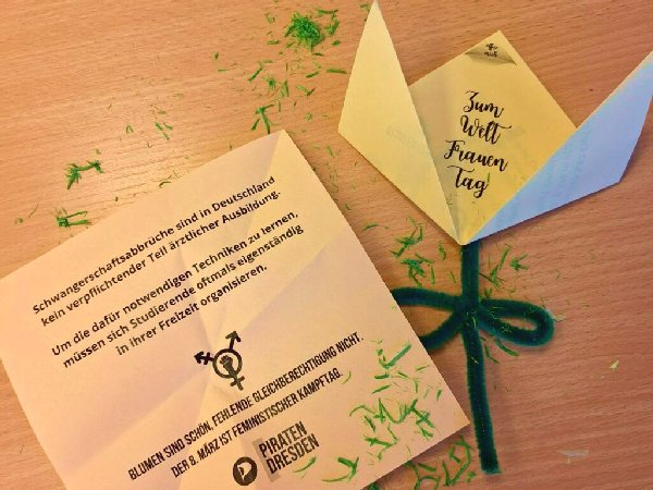 Eine aufgeklappte und eine gefaltete Papierblume nebeneinander. Bei der Aufgeklappten ist zu erkennen, dass sich im inneren Text verbirgt. Dornige_Blumen